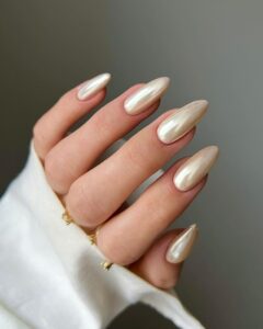 Mão de pele clara, com anéis em dourado e unha amendoada vanilla chrome