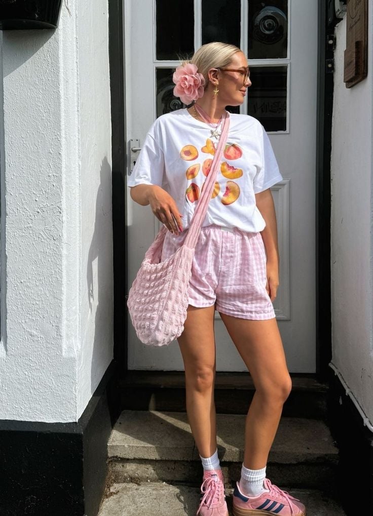 Mulher jovem e magra com pele clara. Ela usa camiseta branca estampada e bermuda.