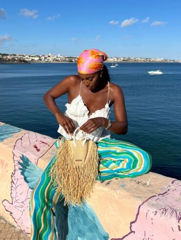 Mulher jovem e magra com pele escura. Ela veste blusa branca de alcinha e calça listrada.