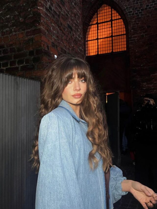 Mulher de pele clara, com roupa azul e cabelo longo escuro ondulado