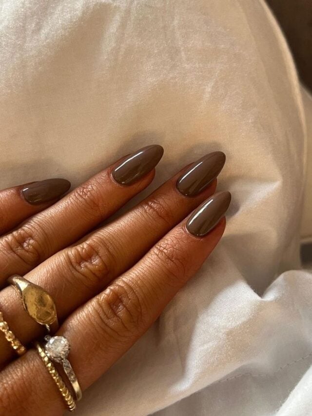 Mão de pele clara-média, com anéis em dourado e unha amendoada Mocha Mousse