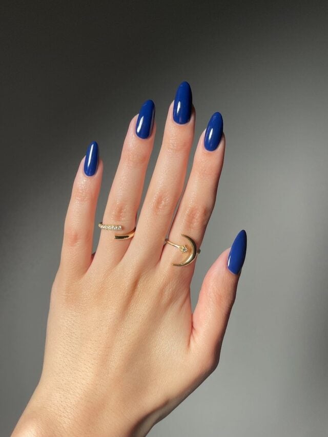 Mão de pele branca, com acessórios em dourado e unha amendoada azul-escuro