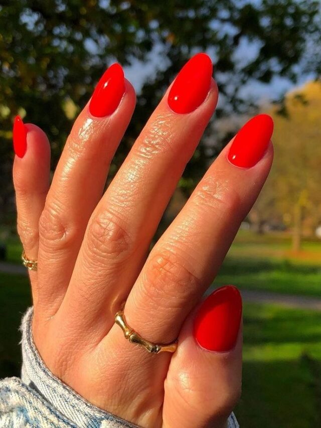 Mão de pele clara, com acessórios em dourado e unha amendoada vermelho-tomate