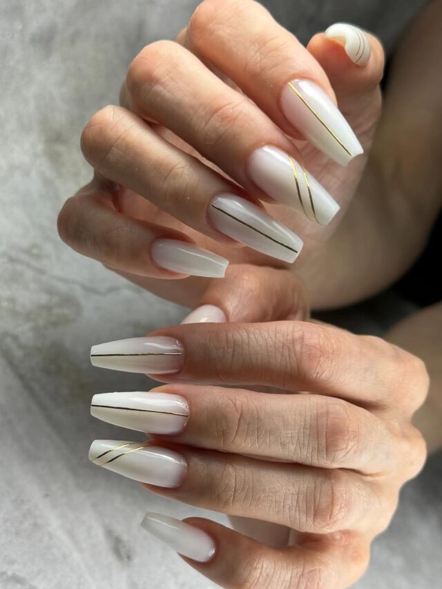 Mão de pele branca, com unha grande em formato quadrado, com nail art minimalista com linhas na cor dourado