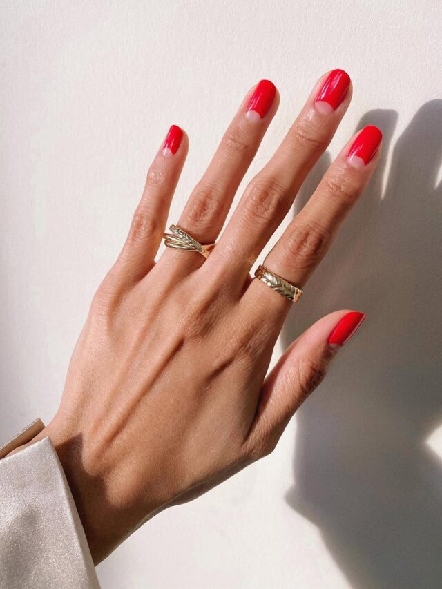 Mão de pele branca, com unha curta e redonda usando esmalte vermelho, com nail art cut out
