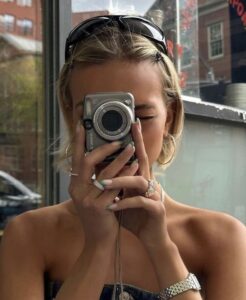 Mulher jovem de pele clara e cabelois loiros tirando foto com câmera cybershot
