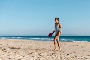 Mulher jovem, magra e branca praticando tênis na praia.