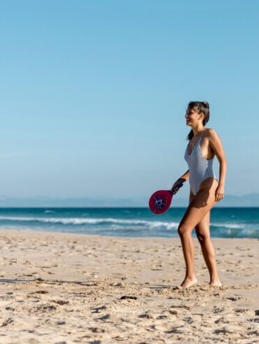 Mulher jovem, magra e branca praticando tênis na praia.
