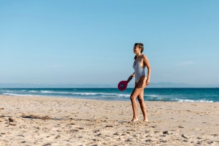 Mulher jovem, magra e branca praticando tênis na praia.