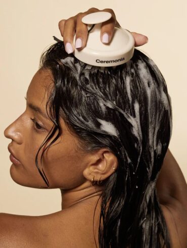Mulher de pele preta-clara, com cabelo escuro. Ela está massageando o cabelo com um escova de limpeza