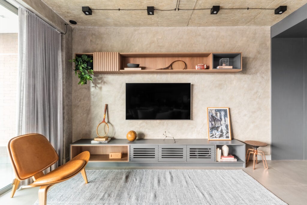 Sala com rack cinza, prateleira e poltrona na cor caramelo