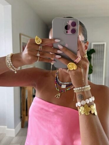Mulher de pele 'média', com tomara que caia rosa e acessórios maximalistas coloridos e em dourado