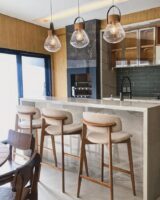 Cozinha com bancada em mármore, pendentes, banquinhos em madeira com assento estofado off-white