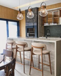 Cozinha com bancada em mármore, pendentes, banquinhos em madeira com assento estofado off-white