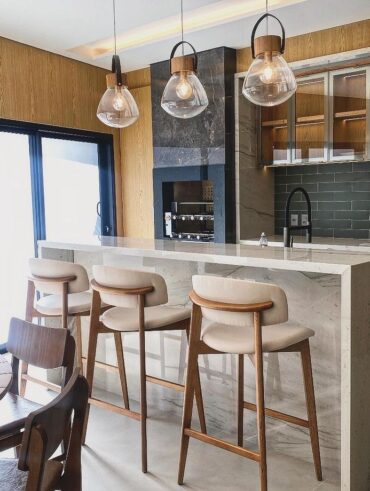 Cozinha com bancada em mármore, pendentes, banquinhos em madeira com assento estofado off-white