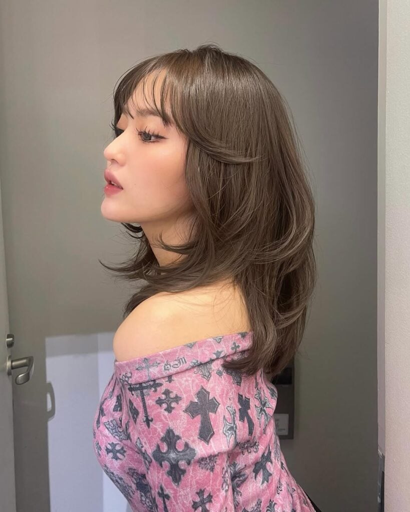 Mulher de pele clara, com descendência oriental, blusa estampada e cabelo castanho com corte gatinho e franja