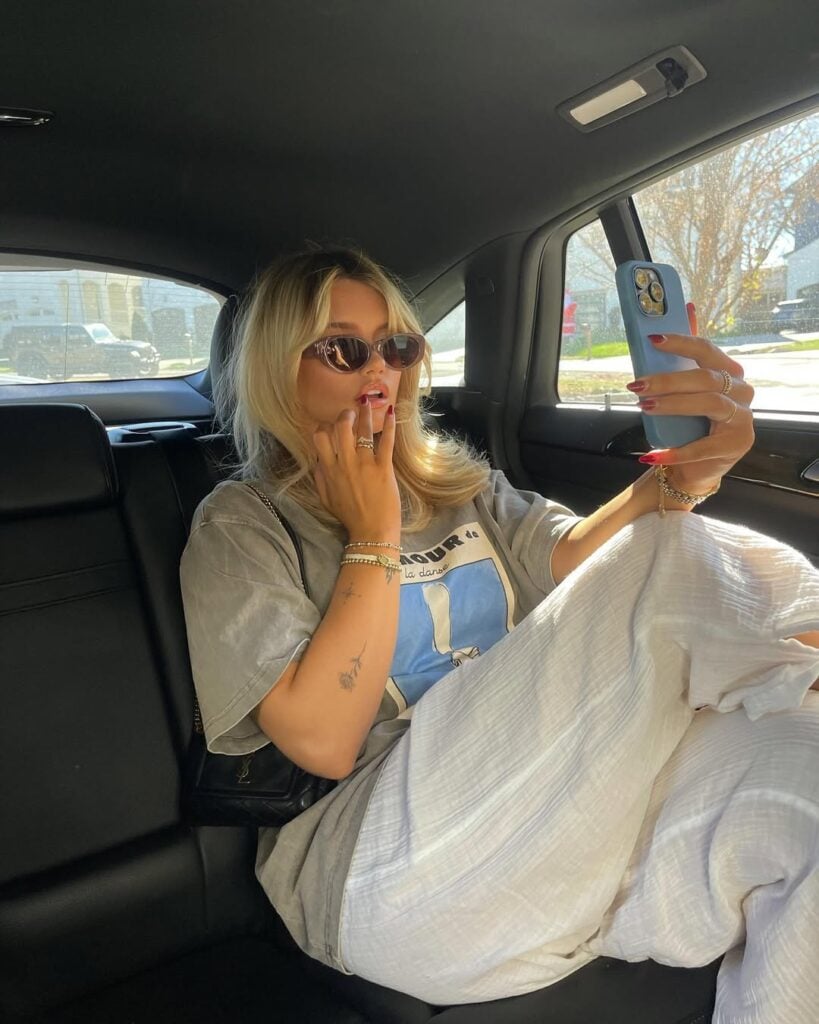Mulher de pele clara sentada no carro, com cabelo loiro e corte gatinho