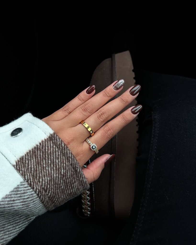 Mão de pele clara, com acessórios em dourado e prata e unha amendoada marrom glazed e com glitter