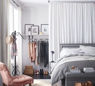 Quarto com cama cinza e closet atrás de uma cortina branca, e poltrona rosa