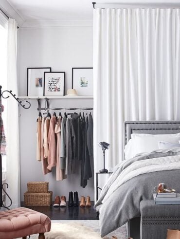Quarto com cama cinza e closet atrás de uma cortina branca, e poltrona rosa