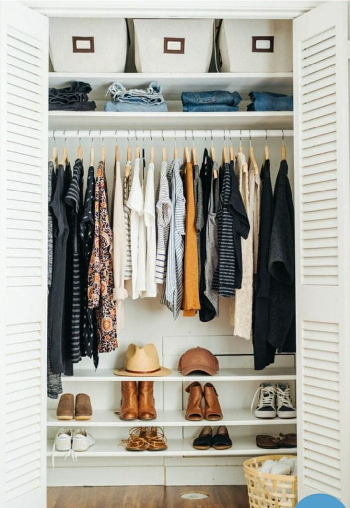 Closet branco com porta de persianas, prateleiras e cabideiros