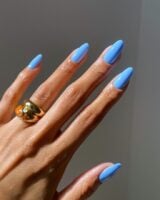 Mão de pele clara, com anel em dourado e unha amendoada azul-céu