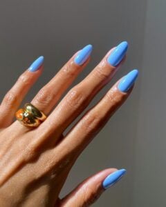 Mão de pele clara, com anel em dourado e unha amendoada azul-céu