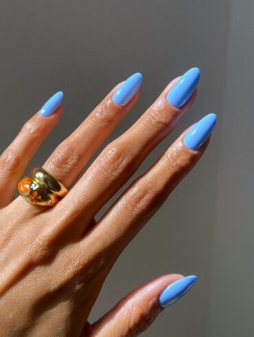 Mão de pele clara, com anel em dourado e unha amendoada azul-céu