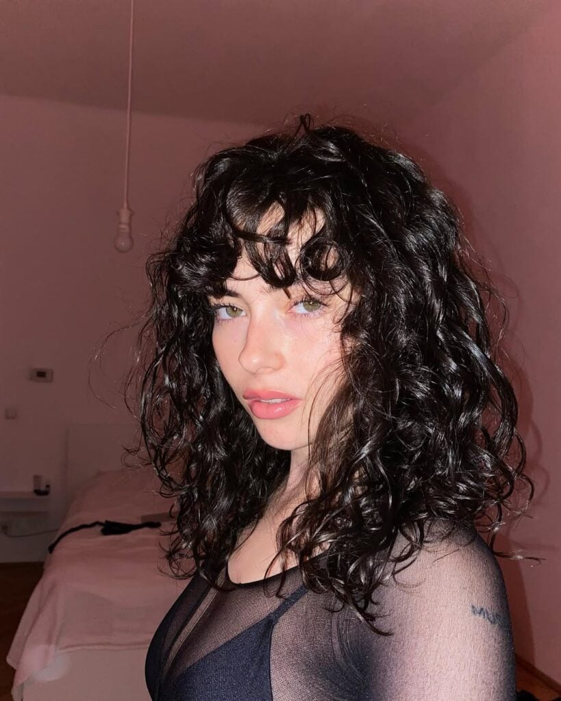 Mulher de pele clara, com look preto e cabelo cacheado escuro com corte gatinho