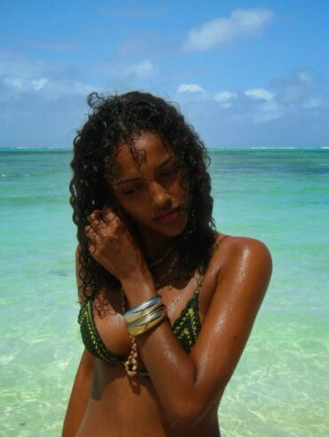 Mulher de pele preta, com biquíni verde e cabelo escuro cacheado