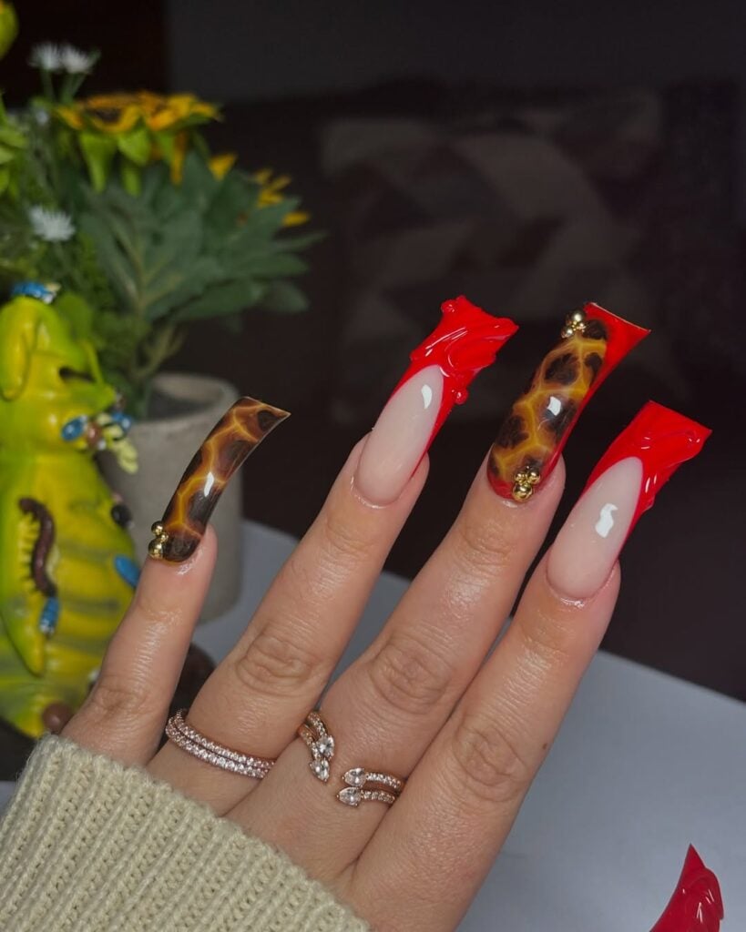 Mão de pele clara, com anéis em dourado e duck nails com francesinha em vermelho com alto relevo e design de tartaruga
