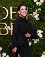 Fernanda Torres, com vestido preto, cabelo solto, acessórios em para e unhas curtas e naturais