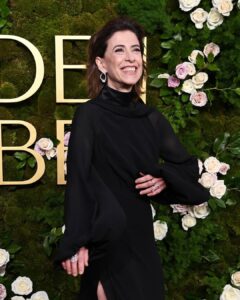 Fernanda Torres, com vestido preto, cabelo solto, acessórios em para e unhas curtas e naturais