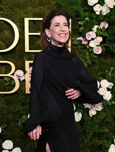 Fernanda Torres, com vestido preto, cabelo solto, acessórios em para e unhas curtas e naturais