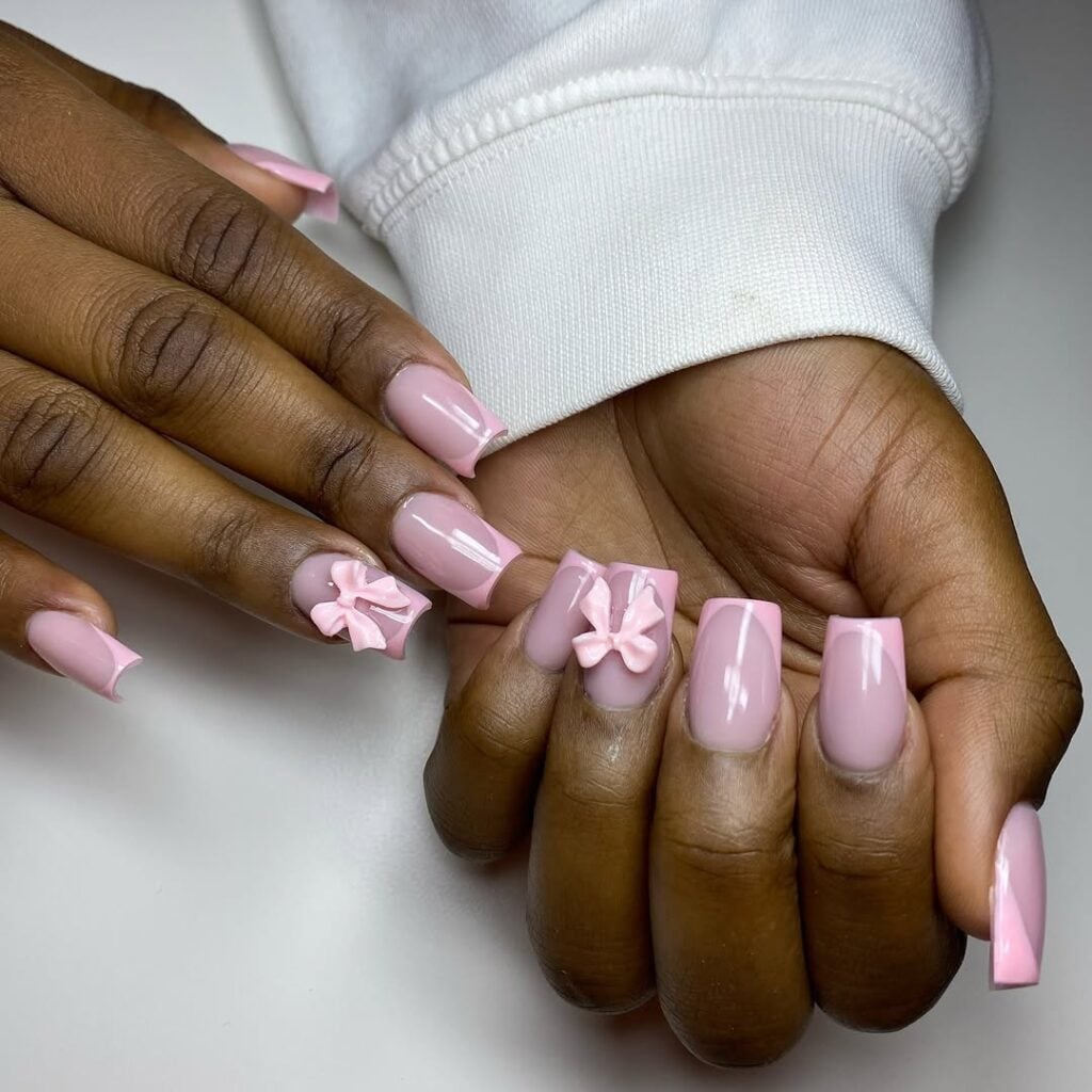 Mão de pele negra, com unha longa e quadrada e esmalte rosa com nail art francesinha e charms de laço
