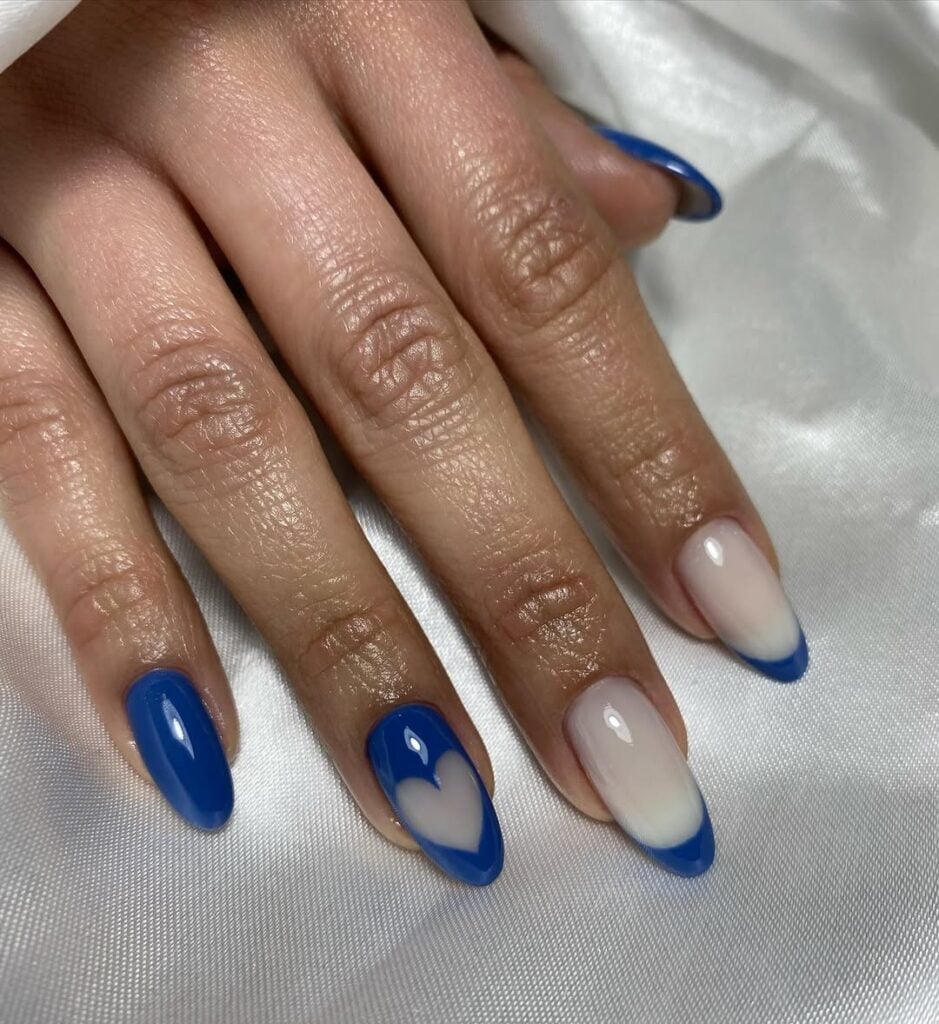 Mão de pele branca, com unha longa e amendoada e esmalte azul com nail art francesinha e coração