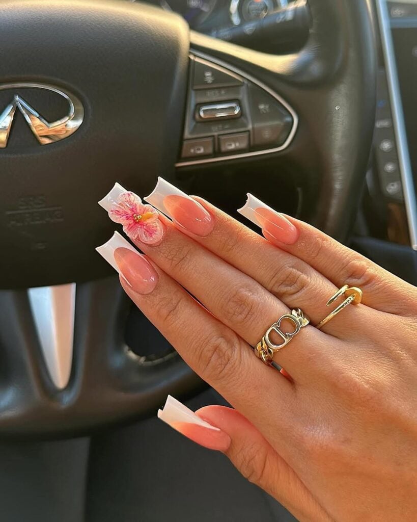 Mão de pele branca, com unha longa e quadrada e esmalte branco com nail art francesinha e charm de flor