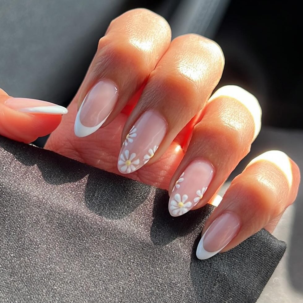 Mão de pele branca, com unha longa e amendoada e esmalte branco com nail art francesinha e flores com amarelo-manteiga