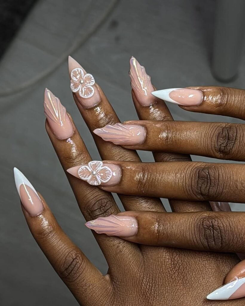 Mão de pele negra, com unha longa e stiletto e esmalte branco com nail art francesinha, de flor e concha