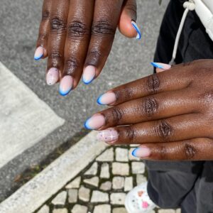 Mão de pele negra, com unha média e amendoada e esmalte azul com nail art francesinha e brilho