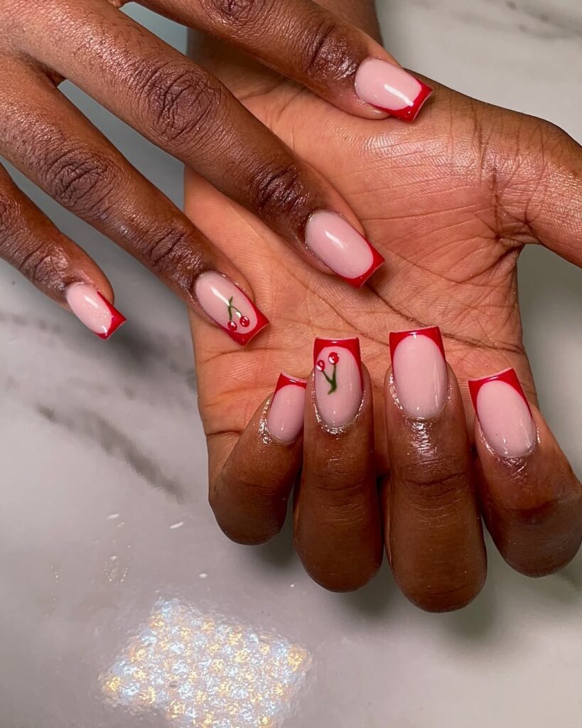 Mãos de pele clara, com unha quadrada com francesinha vermelho-cereja com decoração de cereja