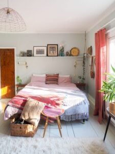 Quarto com cama sem cabeceira e com prateleira com quadros na parede