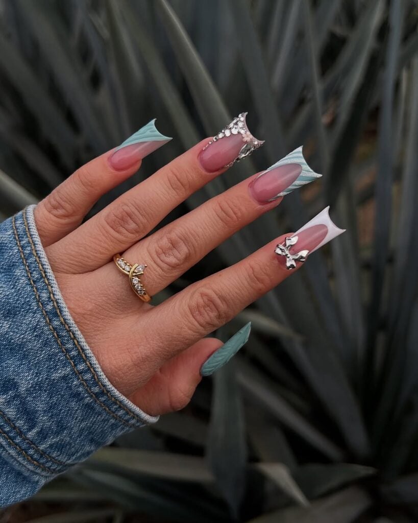 Mão de pele clara, com anel em dourado e duck nail com francesinhas e charms
