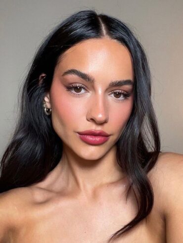 Mulher de pele clara, com cabelo preto ondulado e maquiagem minimalista