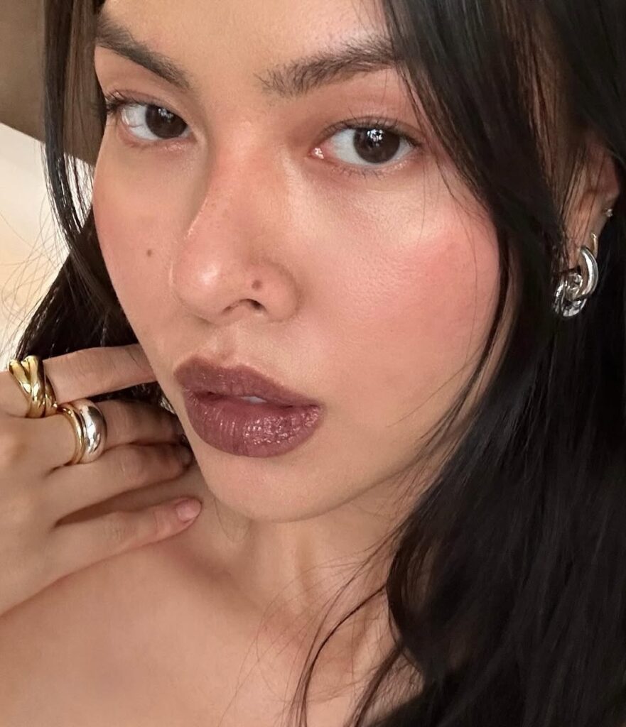 Mulher de pele clara, com cabelo escuro, acessórios em prata e dourado e lábios Mocha Mousse 