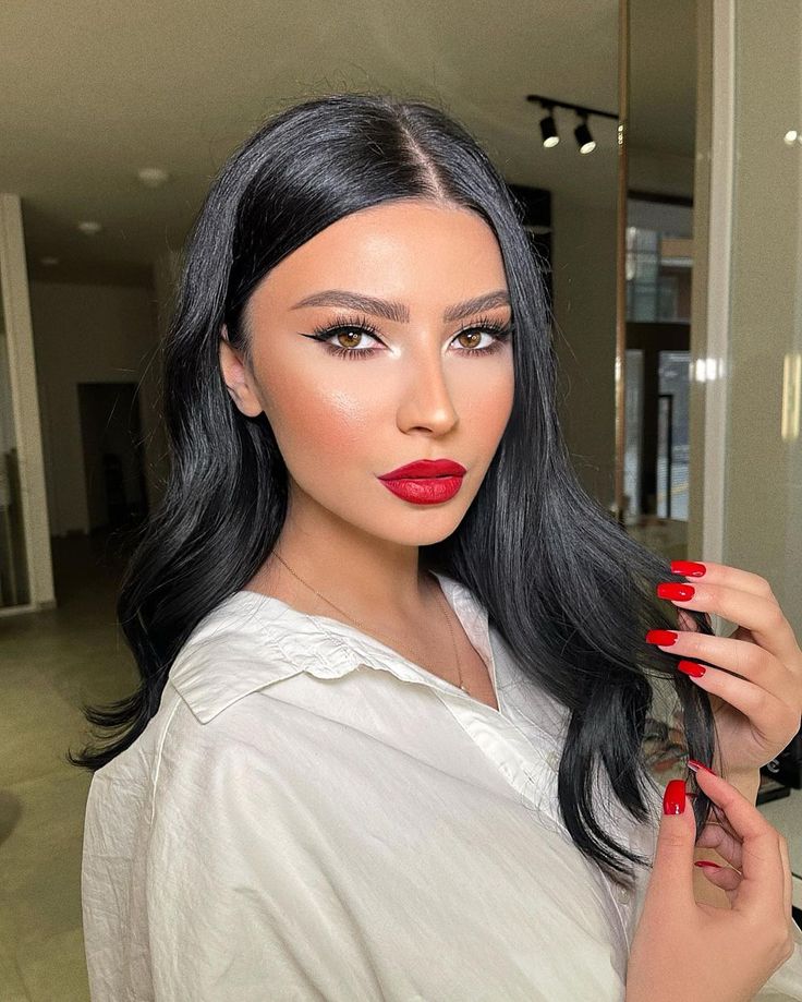 Mulher de pele clara, com blusa branca, cabelo escuro com ondas e maquiagem com batom vermelho 