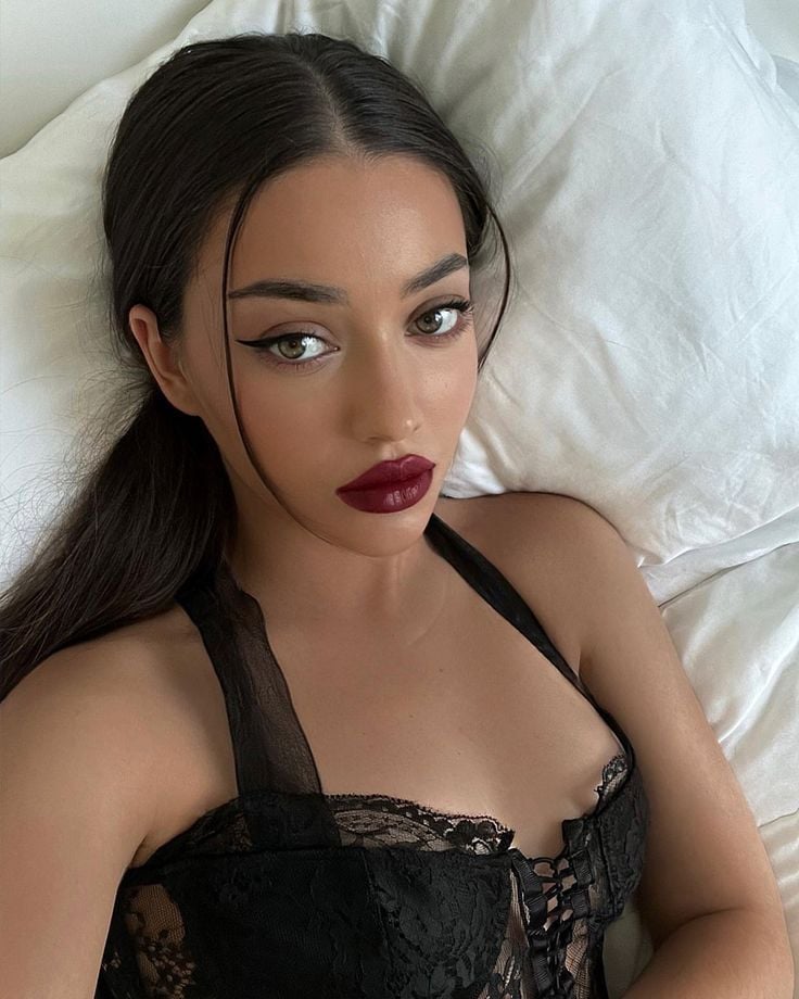 Mulher de pele clara, com corset preto, cabelo escuro preso e maquiagem com batom vinho 
