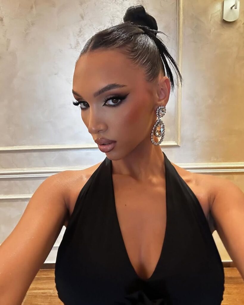 Mulher de pele 'média', com vestido preto, cabelo preso em coque, acessórios em prata e maquiagem com contraste 