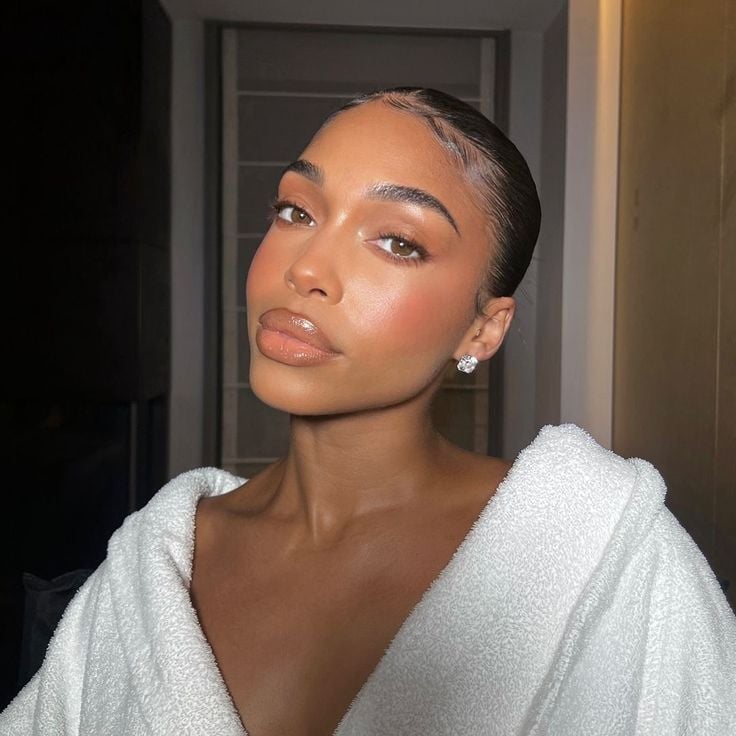 Mulher de pele preta, com cabelo escuro preso, maquiagem com esfumado marrom e roupão branco 