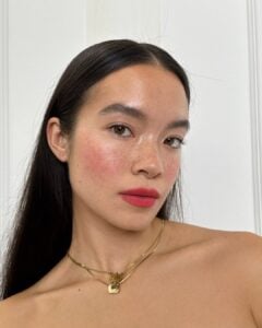 Mulher de pele clara, com cabelo escuro liso, acessórios em dourado e lábios românticos